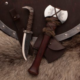 




Here's a gorgeous set of "belt tools" inspired by Norse mythology, attractively stored in an "Asgard Creations" gift/display box.
The Axe:  A handy belt/utility axe with faux fur (no reindeer were harmed in the making of this axe) and leather wrappings. The hardwood handle is replete with nordic runes: Raido (journey), Fehu (wealth), Wunjo (joy), Ehwaz (movement), Naudiz (need), Eihwaz (defense), Teiwaz (warrior), Othila (separate), and Thuisaz (giant). The high carbon steel head is forged from 1055 carbon steel and struck with additional Viking symbols and is thick enough for serious chopping and has a sharp edge. 15" overall; the head is 5" wide with 2-7/8" long cutting edges. Includes leather belt sheath. Weighs 1 lb. 4 oz.
The Knife: Odin didn't have a lap dog, but he did have a pair of shoulder Ravens. Huginn (thought) and Muninn (memory or mind) spied on all of Midgard and reported the daily doings of mankind to the allfather. Unfortunately, a knife handle only has room for one pommel, so you'll have to pick a favorite Raven as you go about your daily business with this knife that would do a hearty Viking proud. The raven head pommel, the guard, and the pommel have a rough-forged finish that looks fresh out of the dwarves' smithy. The carbon steel blade comes sharpened and is easy to resharpen after you've used it for a while. The spine of the blade is 3/16" thick, making this knife suitable for mild chopping as well as precise cutting. With an overall length of 11-1/4" and a 5-3/4" blade, this is a medium-sized knife with a generous handle. The grip is high-quality leather wrapped around a full tang and the raised laces do a superb job of providing a secure grasp in wet situations. Includes leather belt sheath. Wt. 11.7 oz.
The rustic wooden box has leather straps to secure the axe and knife for carrying. Total weight is 7 lbs.




